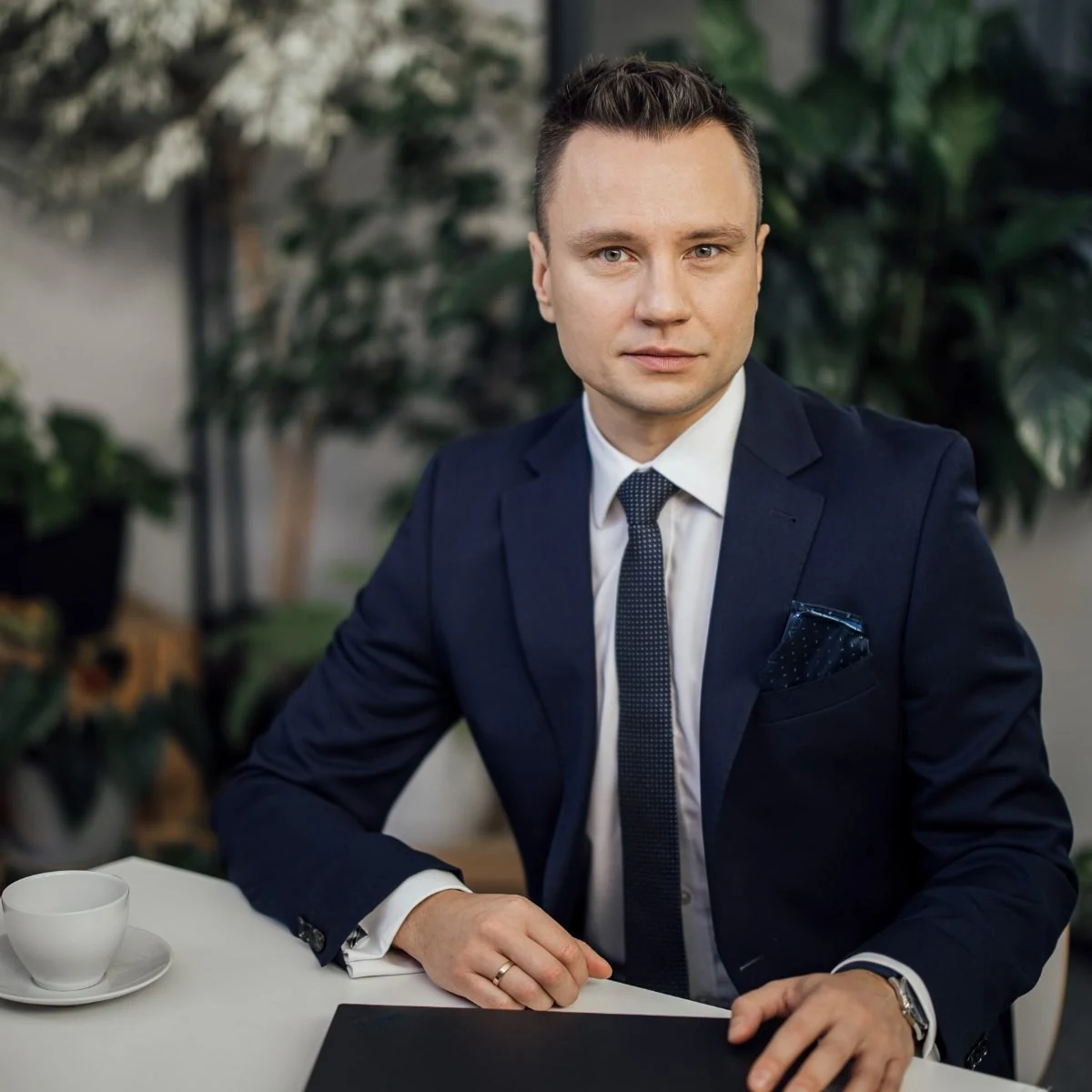 Piotr Sperka przy stole podczas spotkania z klientem, przed nim teczka z dokumentami i filiżanka kawy