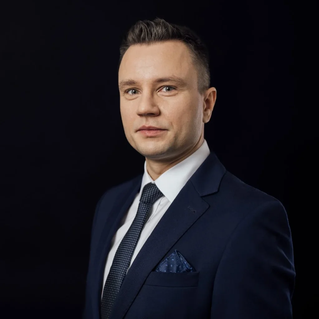 Piotr Sperka, agent ubezpieczeniowy INSOKL, w granatowym garniturze na ciemnym tle