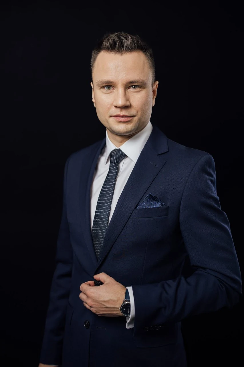 Piotr Sperka, doradca ubezpieczeniowy INSOKL, w granatowym garniturze na ciemnym tle